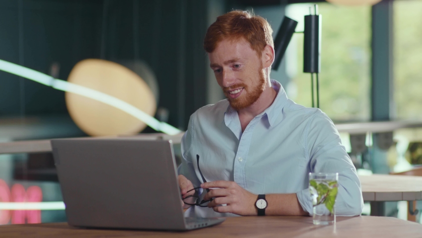Handsome caucasian man using laptop computer communicating remotely with business partners online on distant conference video seminar lecture in the cafe. Royalty-Free Stock Footage #1058675569