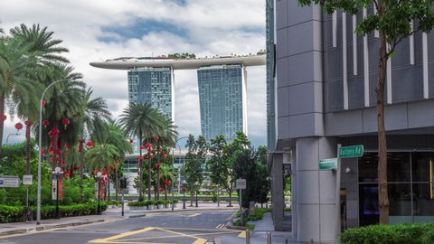 Battery Road avenue with traffic and marina bay on background in downtown timelapse hyperlapse, Singapore. Sidewalk with palms and trees near green lawn. Reflectiion on a glass surface