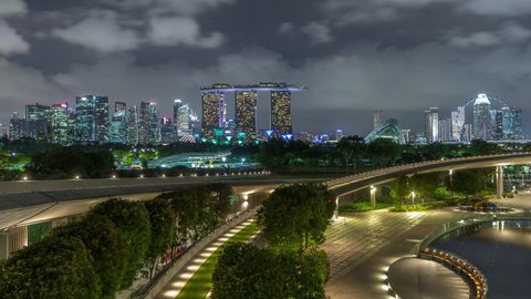 Aerial view Singapore city skyline with colorful fountain at Marina barrage garden night timelapse hyperlapse. Marina barrage has a big fountain in the center and curve walkway lead to the garden.