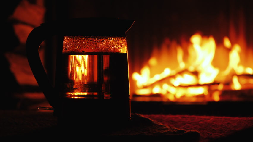 A man turns on the kettle against the background of the fireplace, there the water boils effectively