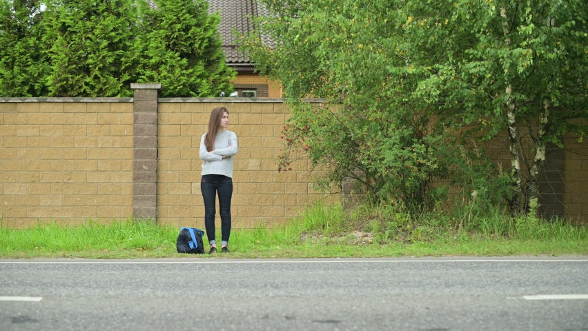 Young woman with travel bag waiting for transport on the side of the country road