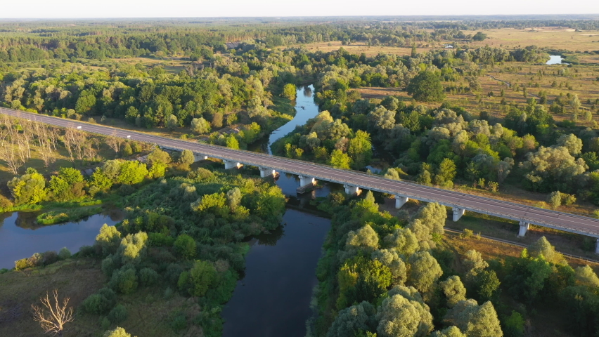 Aerial view of the automobile bridge over the river in the forest. Beautiful morning landscape at sunrise.