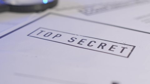 Slow camera pull away from stamped document with Top Secret written on it. Exposed information or secretive material on investigator desk or government agent.