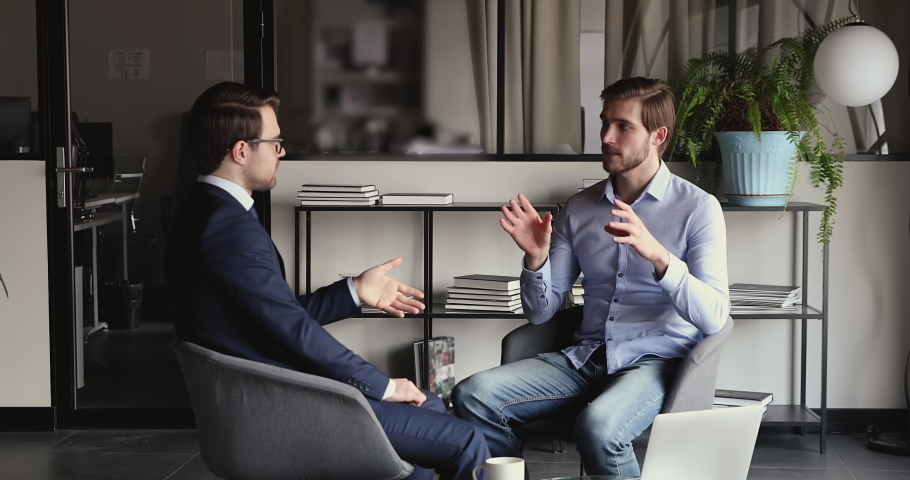 Young confident businessman discussing investment opportunity with financial expert in formal wear, seated on comfortable chairs in office. Smart startup owner consulting with lawyer at meeting. Royalty-Free Stock Footage #1058684281