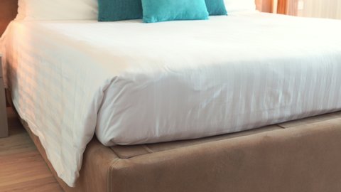 medium wide pan tilt up shot of a modern freshly made resort hotel double bed with white blankets and bedsheets and blue turquise decor pillows ind a beige creme white room interior design.