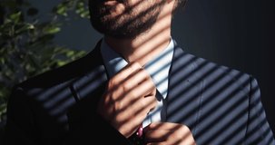 Close up of mature bearded man adjusting trendy tie while standing at modern office. Concept of successful career, business and finance.