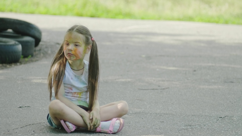 little girl smeared with paint sitting in the Park on the asphalt in the summer at sunset