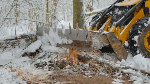 Bulldozer removes a layer of soil in a snowy forest. Construction of the road among the wild
