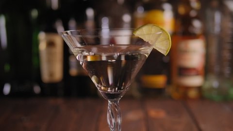 Close-up of the bartender putting a wooden skewer with three green olives in a Martini glass against the background of the bar with various pins. Alcoholic drinks at the bar.