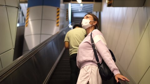 Young woman wearing a protective mask against the virus climbing escalators on public transport  