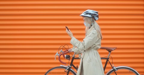 Woman in protective mask, in helmet using her smartphone device, on orange background. 4K video स्टॉक वीडियो