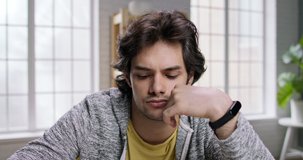 Young caucasian man listening to a lecture or webinar at home. Bored guy resting his head on wrist. Concentrated student focusing on listening - online education 4k footage