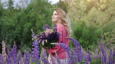 Young pretty woman with a bouquet walks among flowers violet lupins