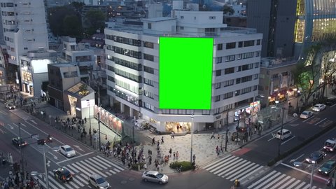 Large billboard with a green screen for advertising, on the modern building, busy crossroad with neon lights, traffic, crowd, Tokyo, Japan. 