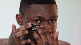 Man skincare. Anti-aging procedure. Portrait of confident african guy applying black hydrogel eye patch isolated on neutral background. Male facial treatment. Metrosexual lifestyle. - Powered by Shutterstock - Get 15% off with code: PIKWIZARD15