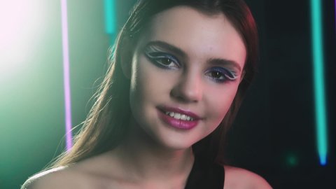 Fashion art. Party look. Happy girl with creative makeup posing smiling in blur neon lights.