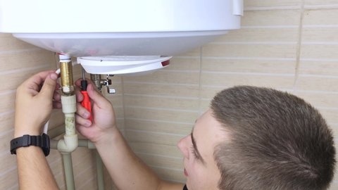 A locksmith fixes a boiler that is not working. The worker will check the electronics and unscrew the nut on the pipe with an adjustable wrench. Technical assistance concept