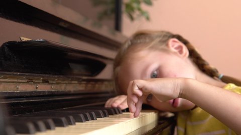 A pretty girl put her head on the piano keys. A little girl plays the piano in a music class.The child is tired of learning a music lesson. 4k