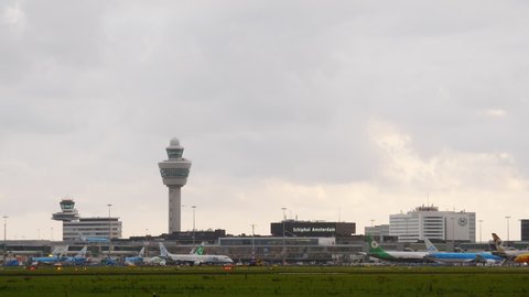 AMSTERDAM - AUGUST 15, 2019: Passenger Flybe plane and and DHL cargo jetliner taxiing against Schiphol airport terminal, telephoto view. Many airliners parked against boarding gates