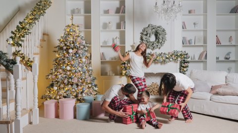 Cheerful family of four in pajamas with gifts in the room are enjoying Christmas, dancing and shaking holiday boxes