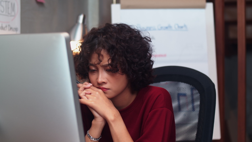 Serious Young Asian Businesswoman in casual clothes working on a desktop computer thinking solving a problem at office workplace. Overworked Concentrated woman working late in office at night.   Royalty-Free Stock Footage #1058723119