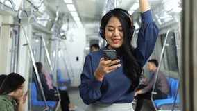 A lifestyle of young Asian woman using cellphone with headset while taking the subway train to work at the rush hour morning