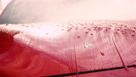 Close up of drops of water flowing on car while worker using a high-pressure water sprayer washing car.