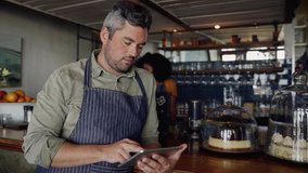 Clip of handsome cafe owner scrolling on tablet while beautiful female make coffee. 