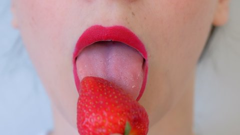 Woman with sensual red lips and freckles eating strawberry on white background, lips closeup. She sexy licks a berry her tongue before eating it. Vitamins from fresh strawberry. Unrecognizable girl.
