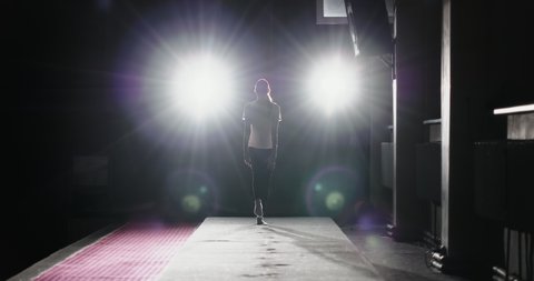 The girl gymnast runs in a straight line gaining momentum before the jump. Makes a jump push flip forward in a dark gym with single bright spotlight.