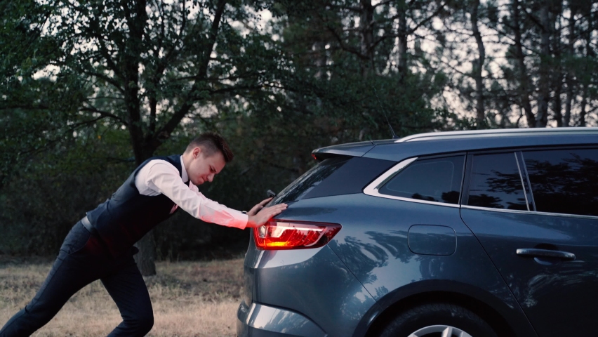 Side view of a Man pushing broken car, vehicle with trouble. young Man in business suit pushing a broken car.  Pushing a broken down car