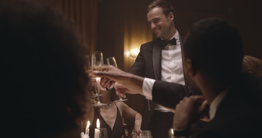 Happy friends toasting with wine at gala night party. Group of men and women celebrating with drinks at dinner party.
 | Shutterstock HD Video #1058735074