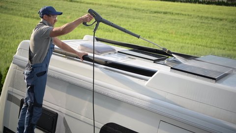 Male RV Owner Cleaning Roof Of Vehicle With Pressure Washing Wand By Carefully Spraying Water On Solar Panels And Skylight Window.