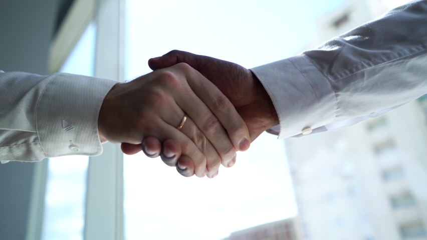 Close-up of handshaking of two unrecognizable partners African American business man and Caucasian businessman background of window and office building in sunny day. Tracking shot in slow motion. | Shutterstock HD Video #1058737057