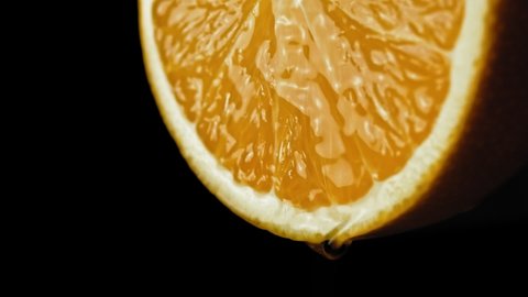 sliced orange fruit with drops of juice falling from it in slow motion. Closeup macro shot. Fresh berry and fruit series.