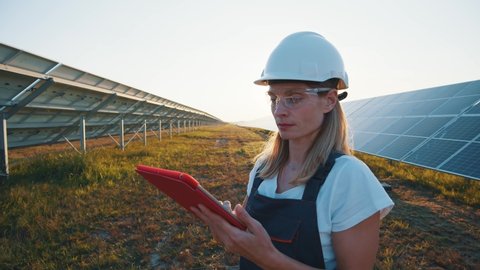 Professional woman engineer using tablet computer for maintenance on ecological gree field with solar panels. Photovoltaic power station. Female worker.