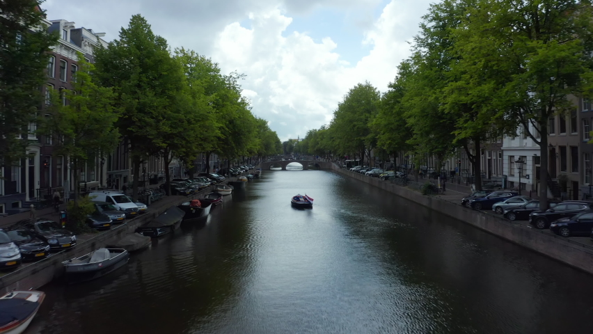 Amsterdam Canal with Boat and Dutch Flag waving in wind, forward Aerial  | Shutterstock HD Video #1058741530