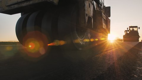 A grunge road roller levels the asphalt in the setting sun. Road surface repair. Construction of a new road. Road construction machines. A layer of freshly laid asphalt.