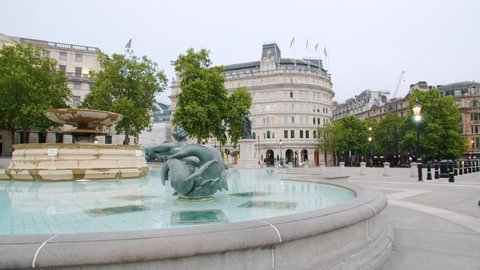 Lockdown in London, Slow motion Gilmbal pan of Empty Trafalgar Square fountain during coronavirus pandemic 2020, with one lone police car & flying birds.