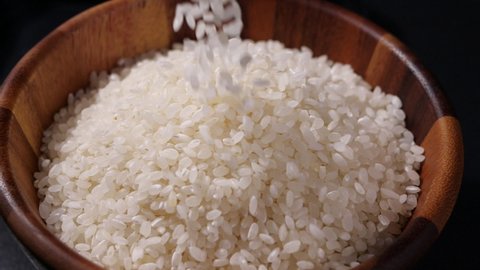Japanese rice falling in slow motion. Raw rice grain in wooden bowl