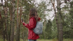A young Caucasian woman in a coronavirus mask is vlogging in the forest. A woman the forest communicates on a video call using a smartphone.