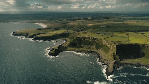 Aerial Ireland green farmlands: ocean gulf with stony shore. Amazing farms and cottages at wide greenery Irish cereal fields, grassy valleys and meadows. Cinematic footage shot