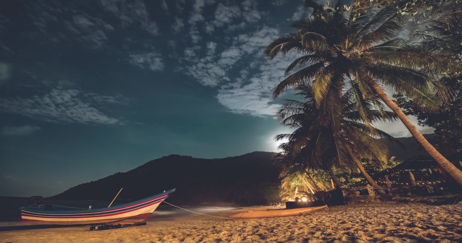 Boat at sand ocean beach timelapse at night scenery of Koh Phangan Island, Thailand, Asia. Magnificent landcape with tropical palms and mountains silhouette. Nobody cinematic shot