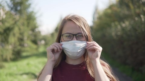 Woman in glasses at the street puts on medical mask. Mask using during corona virus pandemic and quarantine.