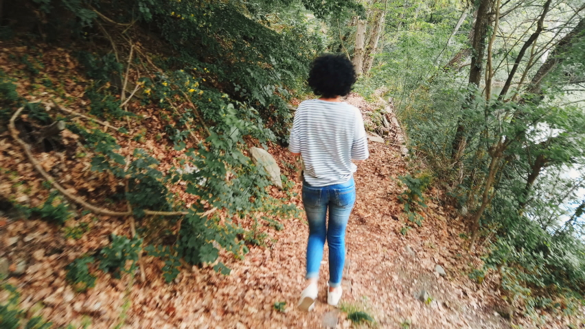 Young beautiful woman walking through a pathway in forest along the lake with soft natural lighting