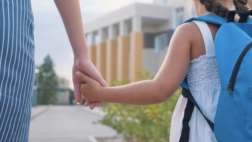 Happy family mom and daughter go hand in hand. A woman and a girl with a backpack behind them. Happy little girl dreams of school. Dreaming little girl goes with mom to school for the first lesson Royalty-Free Stock Footage #1058762155