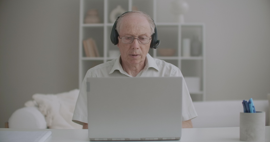 aged male professor is communicating by video call from home, using laptop and headphones Royalty-Free Stock Footage #1058763823