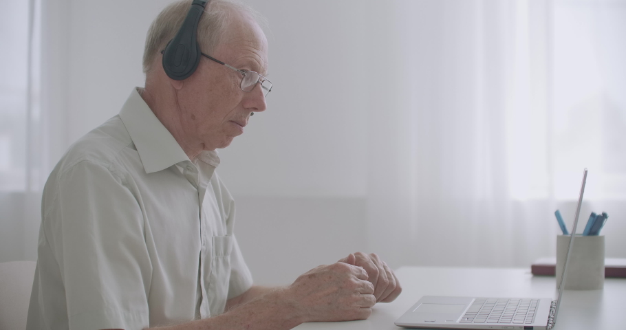 Aged professor is explaining to pupils lecture, communicating online, by webinar and video call, sitting at home | Shutterstock HD Video #1058763916