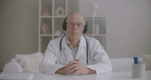 elderly male therapist is listening patient during online consultation, nodding head, portrait of physician
