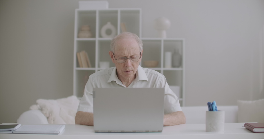 elderly man is working with laptop at home, typing message and checking email, remotely job for retiree Royalty-Free Stock Footage #1058763970